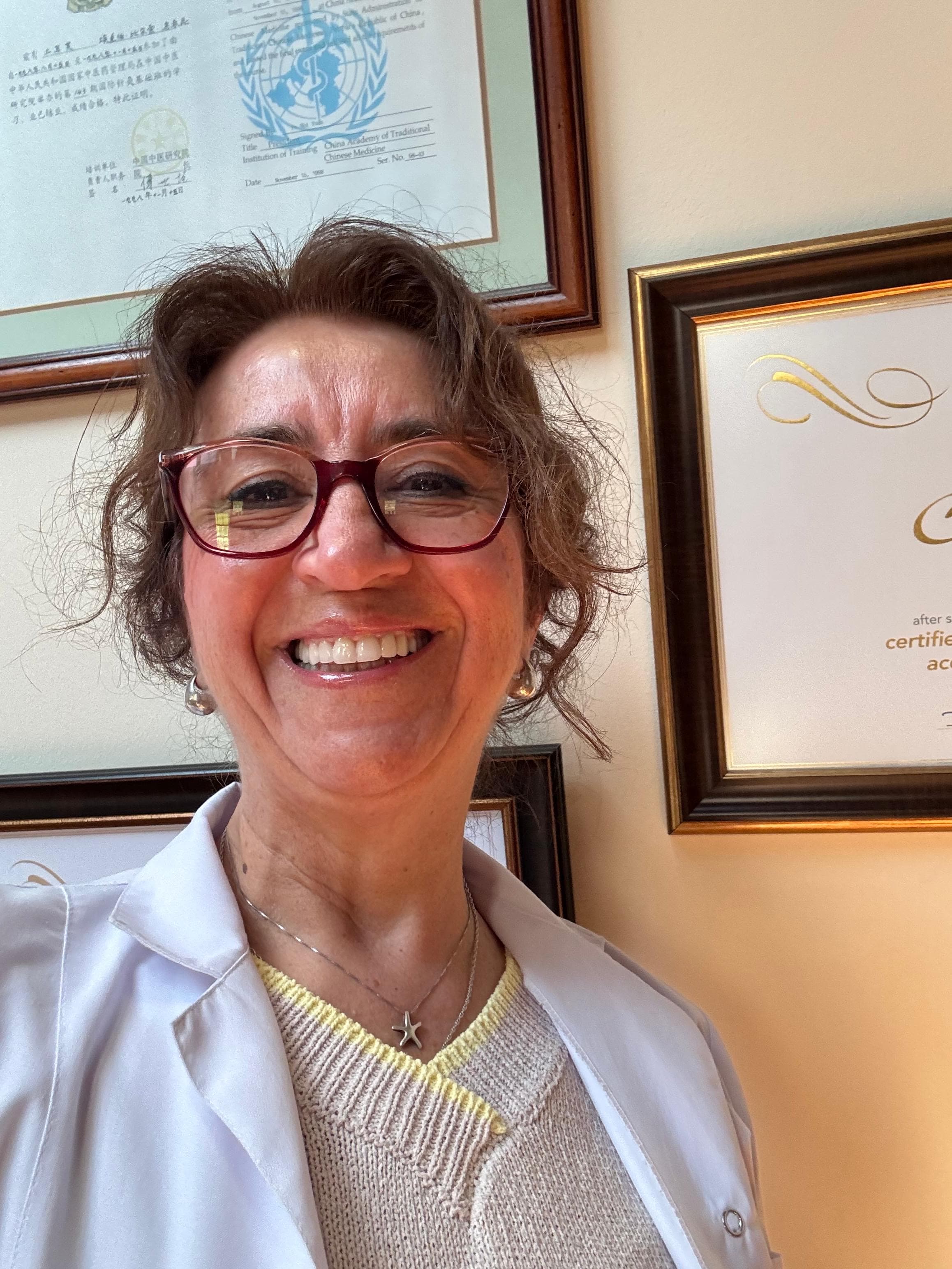 Dr. Birsel Uçkun smiling in her clinic surrounded by professional certificates